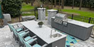 Picture of an outdoor kitchen with a grill, a sink, cabinets, countertops, and chairs.