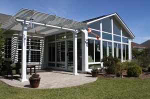 A home exterior features a pergola over a paver patio and an attached sunroom.