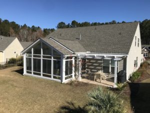 The exterior of a single-family home with a shingle roof that has an attached sunroom and pergola.